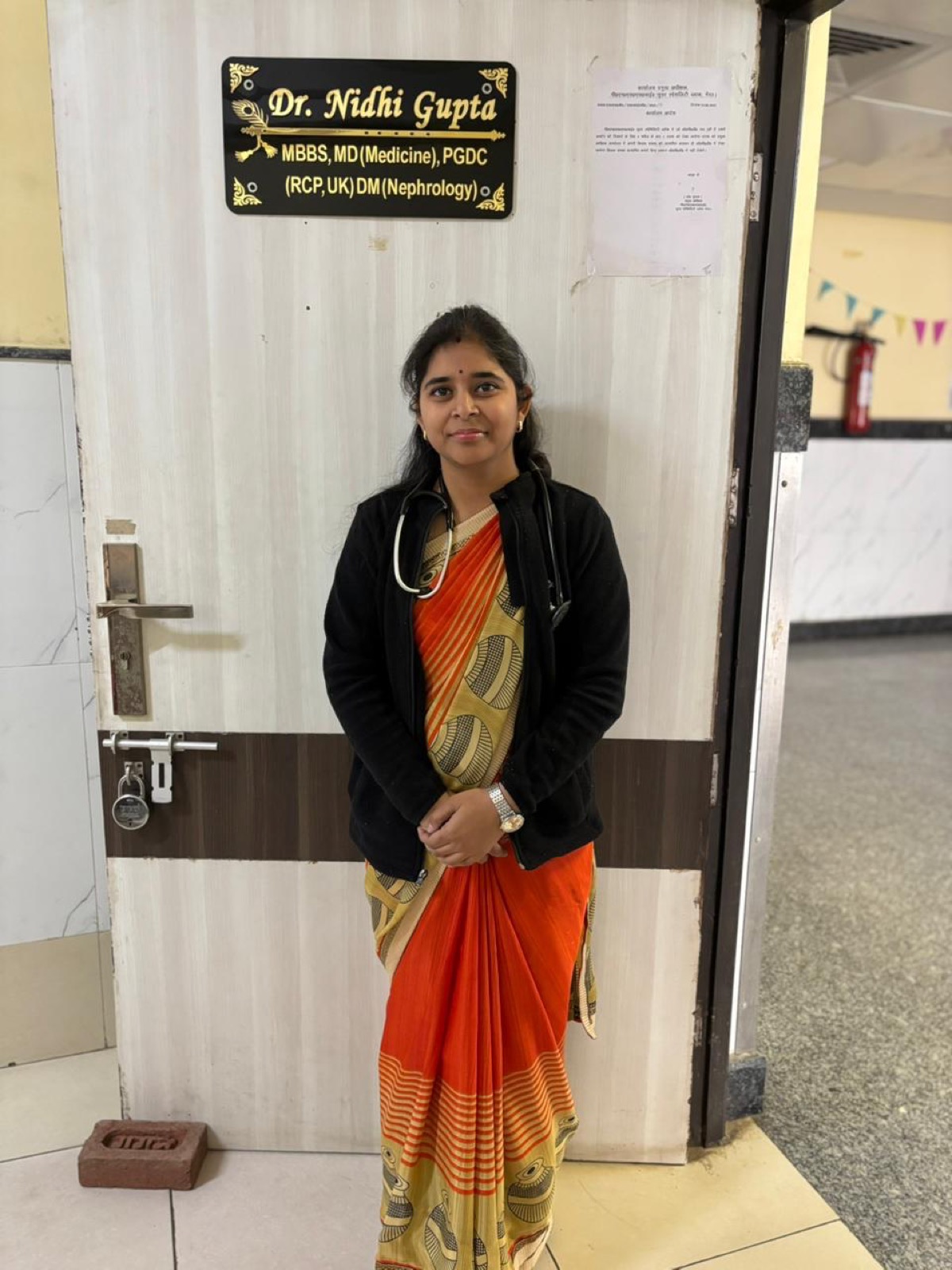 Dr. Nidhi Gupta outside her nephrology clinic in Gurugram — nameplate showing MBBS MD DM Nephrology credentials